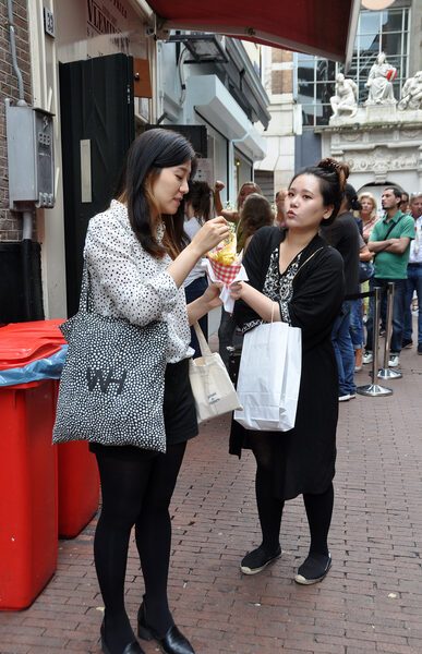 Two friends sharing a red gingham cone of Vleminckx fries in front of the shop